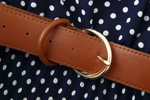 Detail of brown leather belt with gold buckle on navy blue polka dot midi dress