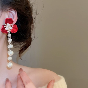 Close-up of elegant red flower earrings with delicate pearl tassels worn by a model
