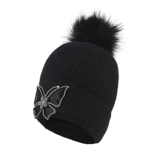Women's black knit beanie featuring a faux fur pompom and a sparkling rhinestone butterfly