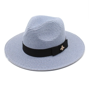 Detail of blue straw fedora hat featuring black ribbon and gold bee metal buckle ornament