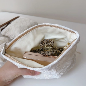 Close-up of white lace embroidered cosmetic pouch showing metal zipper and inner storage