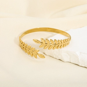 Detailed shot of golden leaf-shaped open bangle on white stone and beige fabric