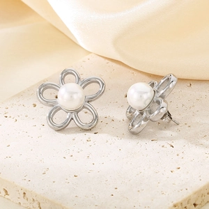 Detailed view of floral stud earrings with white pearls on a textured beige background