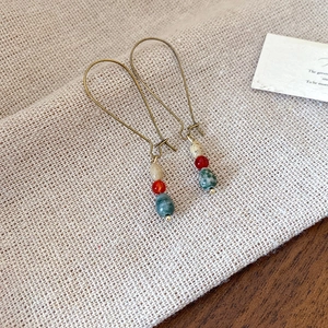 Macro shot of ethnic style drop earrings with red and green stone beads on linen