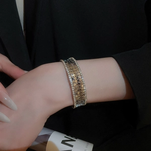 Detail of gold wide layered cuff bracelet with zircon edges and scale texture on blazer