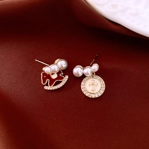 Detail of asymmetric pearl earrings with red horse charm and golden cross pendant