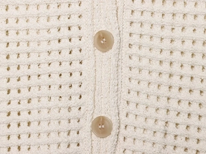Detailed macro view of cream knitted cardigan fabric with hollow mesh texture and amber buttons