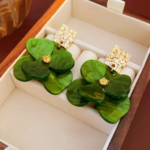 Macro shot of green acrylic flower earrings with golden hammered metal studs in a jewelry box