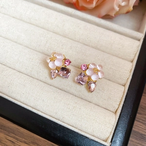 Detail of flower earrings with pink petals, crystals, and gold accents on a jewelry tray