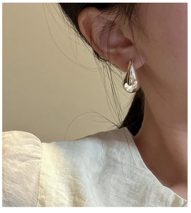 Close-up of polished silver teardrop earrings worn by a model in warm lighting