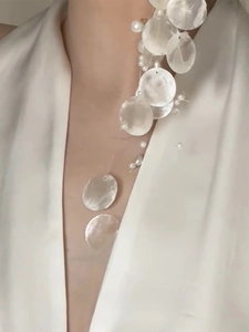 Detailed view of white shell and pearl tassel necklace drape on a model's neck