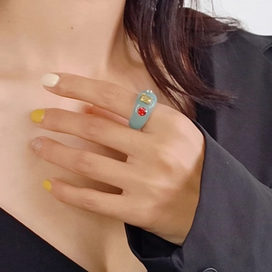 Close-up of a teal resin wide band ring featuring square gold and round red inset stones