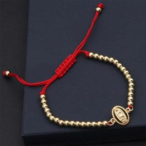 Close-up of a red woven bracelet with gold beads and a Virgin Mary religious pendant