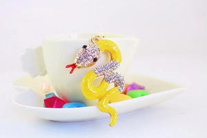 Detail of yellow enamel snake keychain with rhinestones hanging on a white teacup