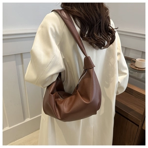 Brown litchi grain leather hobo bag worn as a shoulder bag in a minimalist setting
