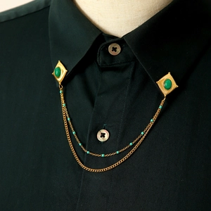 Dettaglio catena per colletto vintage dorata con pietre verdi su colletto di camicia