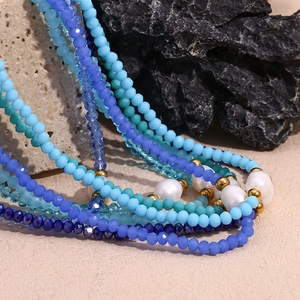 Blue crystal beaded necklace with freshwater pearls and gold accents on stone background