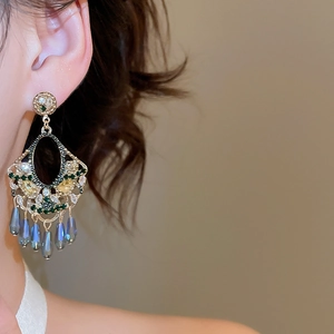 Close-up of vintage gold tassel earrings with green and blue stones on ear