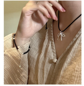 S925 silver bow pendant necklace and beaded heart bracelet on a linen fabric background