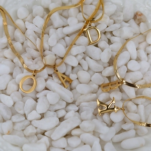 18K gold plated snake chain necklaces with initial pendants on white pebbles