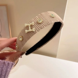 Dettaglio del cerchietto in velluto a coste albicocca con perle a forma di H e strass