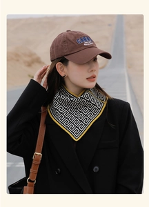 Detail of a brown baseball cap with embroidery paired with a geometric silk scarf