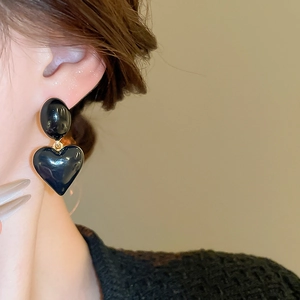 Close-up of elegant black heart drop earrings with gold metallic trim worn by model