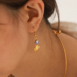 Gold tropical fish earrings with blue porcelain beads worn by model for beach style