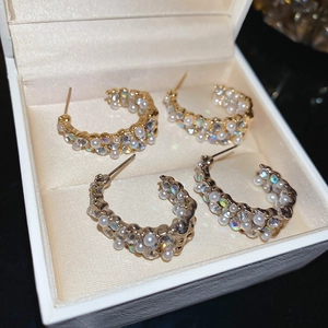 Close-up of elegant C-shaped earrings with pearls and crystals in gold and silver plating