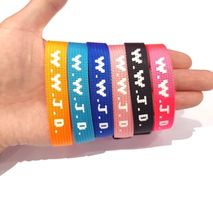 Close-up of hand holding six colorful woven W.W.J.D. adjustable fabric bracelets