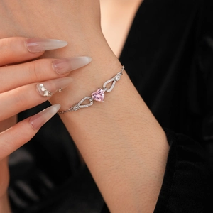 Detail of female wrist wearing a silver bracelet with pink heart-shaped zircon and droplets