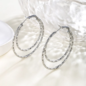 Macro detail of silver double-layered hoop earrings with intricate textured chain pattern