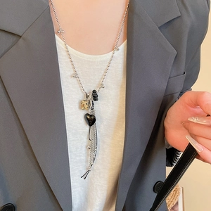 Dettaglio collana a sfere argento con cuore nero e ciondolo a cubo su una giacca blazer