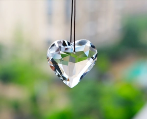 Macro view of a clear multifaceted heart crystal pendant hanging in outdoor sunlight
