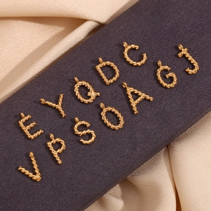 Macro detail of 18K gold plated twisted texture alphabet pendants on silk fabric