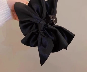 Dettaglio di una grande molletta per capelli con fiocco in raso nero tenuta in mano