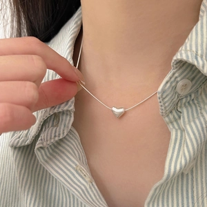 Close-up of a silver heart-shaped pendant necklace worn on a blue striped shirt