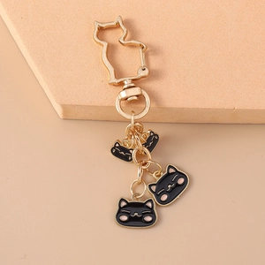 Detail of gold metal cat keychain with three black enamel kitten pendants on pink background
