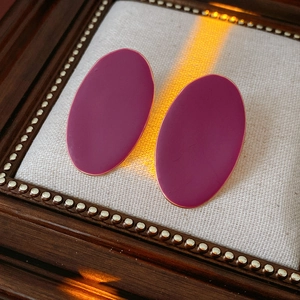 Dettaglio di orecchini ovali viola con bordo dorato su tessuto beige in scatola