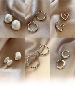 Detail view of six geometric silver earrings on silk fabric showcasing various modern shapes