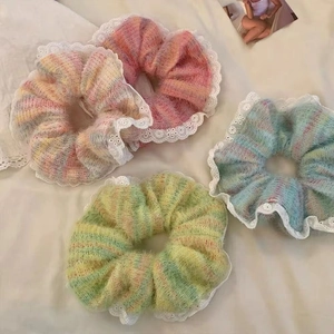 Set of four colorful plush scrunchies with white lace edges on beige fabric background