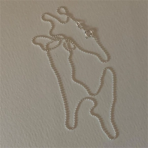 Minimalist 925 sterling silver ball chain necklace laid on a beige textured background