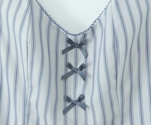 Detail of V-neckline with blue lace trim and ribbon bows on striped fabric
