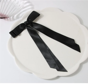 Détail d'un nœud papillon en satin noir avec de longs rubans sur un plateau en céramique
