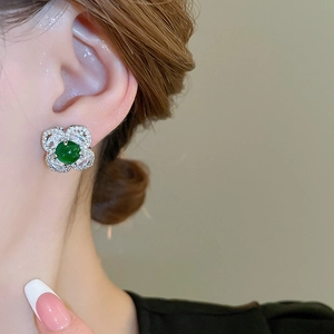 Close-up of vintage flower stud earring with emerald gemstone and diamond petals on ear