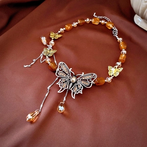 Close-up of tiger eye beaded necklace with silver butterfly pendant on brown velvet