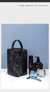 Macro shot of black textured PU leather travel wash bag on marble surface with accessories