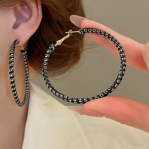 Détail macro de créoles dorées avec insert en cuir noir et impression du mot NICE