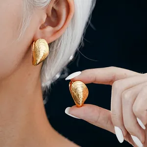 Golden shell-shaped metallic earrings with ribbed texture worn by a model in a close-up view