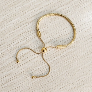 Waterproof gold snake chain bracelet with adjustable slider and tassel ends on wood